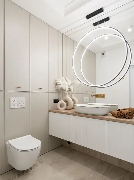 Nowoczesna łazienka z jasnymi meblami, oświetleniem i dekoracjami.