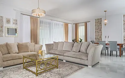 Wnętrze salonu w stylu glamour i quiet luxury z beżową sofą i złotymi akcentami.