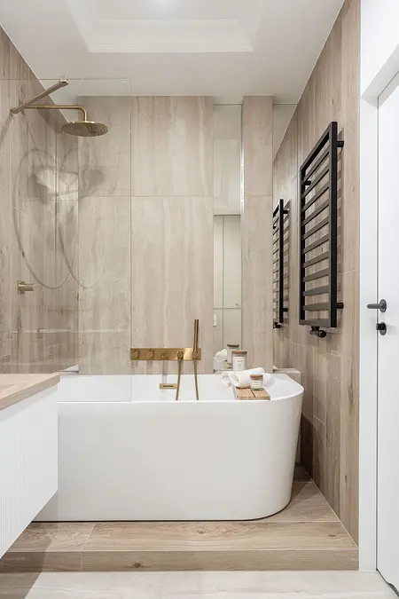 Nowoczesna łazienka z wanną, drewnianymi detalami i złotymi akcentami.