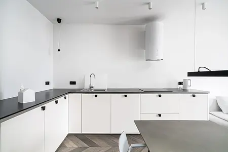 Kuchnia w minimalistycznym stylu z białymi meblami i czarnym blatem.
