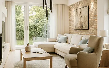 Wnętrze salonu w stylach eklektycznym i minimalistycznym z jasną sofą i ceglaną ścianą.