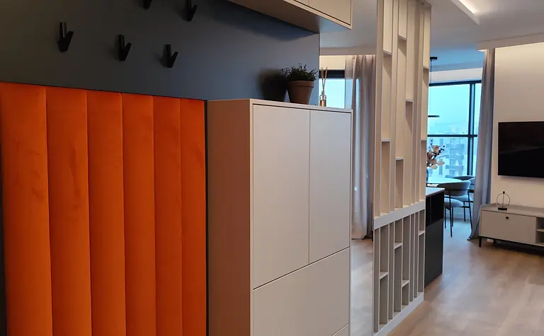 Przedpokój w stylu minimalistycznym z pomarańczowym siedziskiem i białymi meblami.