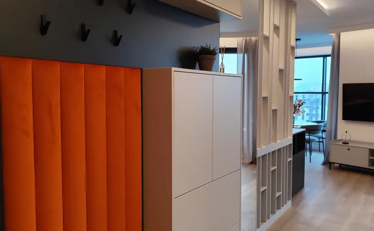 Przedpokój w stylu minimalistycznym z pomarańczowym siedziskiem i białymi meblami.