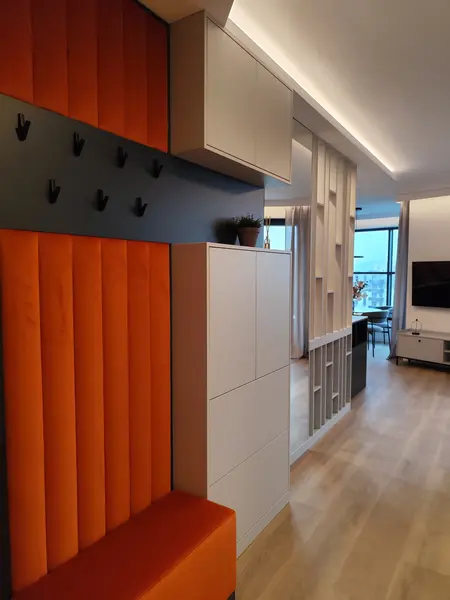 Przedpokój w stylu minimalistycznym z pomarańczowym siedziskiem i białymi meblami.
