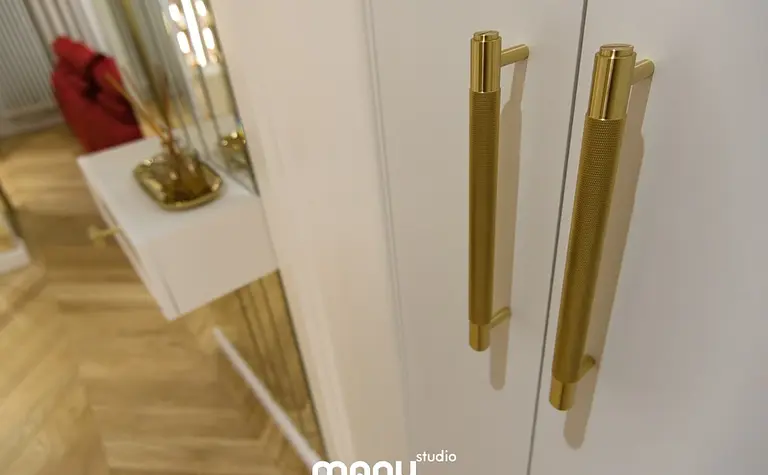 Nowoczesne wnętrze z białymi meblami, złotymi akcentami i drewnianą podłogą.