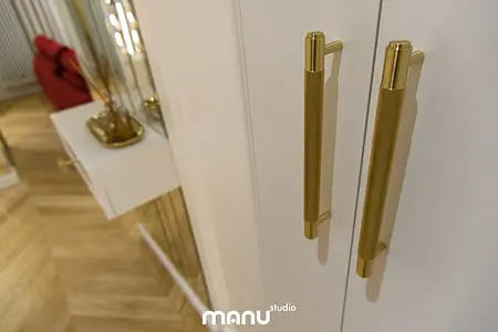 Nowoczesne wnętrze z białymi meblami, złotymi akcentami i drewnianą podłogą.