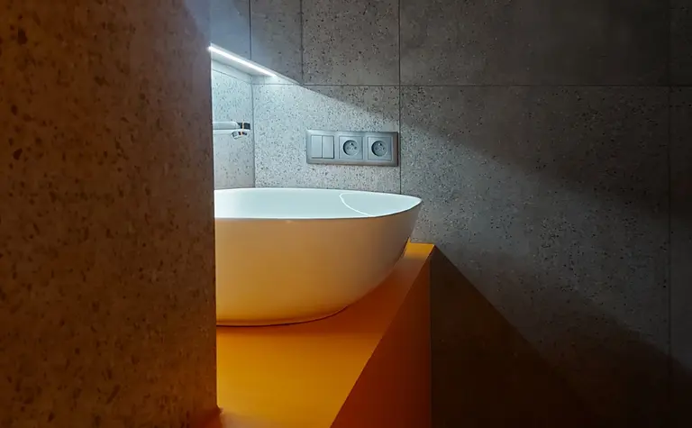 Wnętrze łazienki z białą umywalką na pomarańczowej szafce w stylu industrialnym.