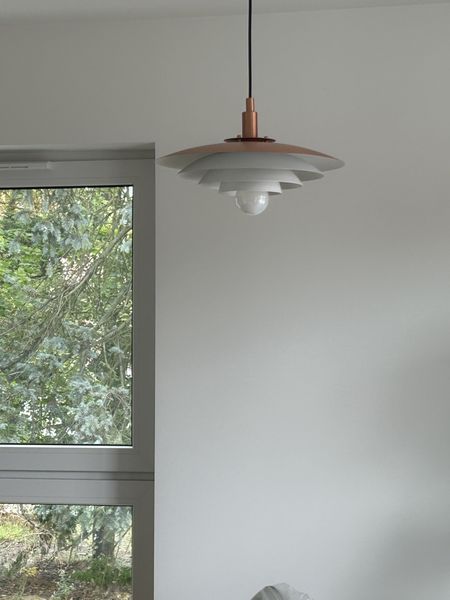 Lampka sufitowa w minimalistycznym wnętrzu z białymi ścianami i dużym oknem.