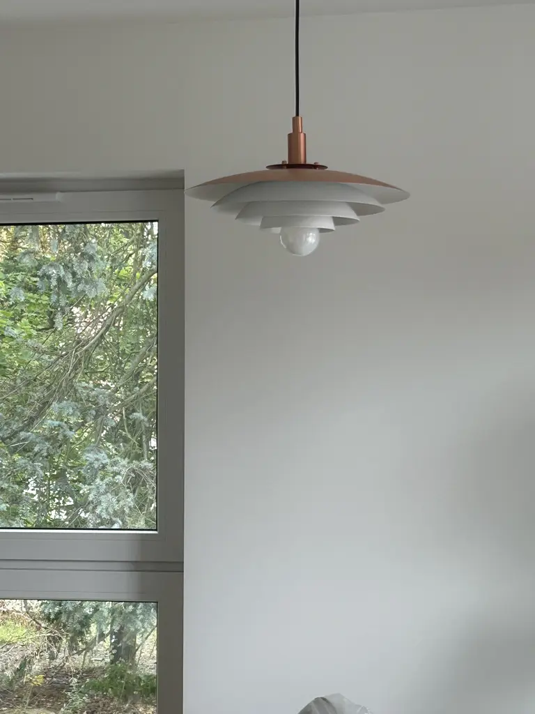 Lampka sufitowa w minimalistycznym wnętrzu z białymi ścianami i dużym oknem.