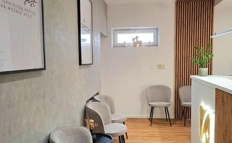 Przestronne wnętrze biura z szarymi fotelami, drewnianą dekoracją i nowoczesnym oświetleniem.