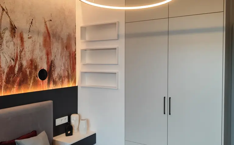 Sypialnia w stylu minimalistycznym z nowoczesnym oświetleniem i szafą.