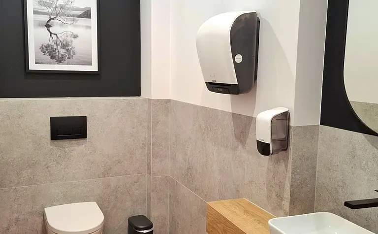 Toaleta z szarymi płytkami, drewnianym blatem, lustrem i nowoczesnym wystrojem.