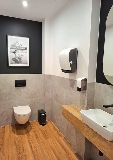 Toaleta z szarymi płytkami, drewnianym blatem, lustrem i nowoczesnym wystrojem.