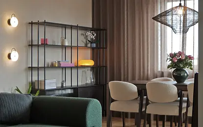 Wnętrze jadalni z zieloną sofą, drewnianym stołem i nowoczesnymi lampami.