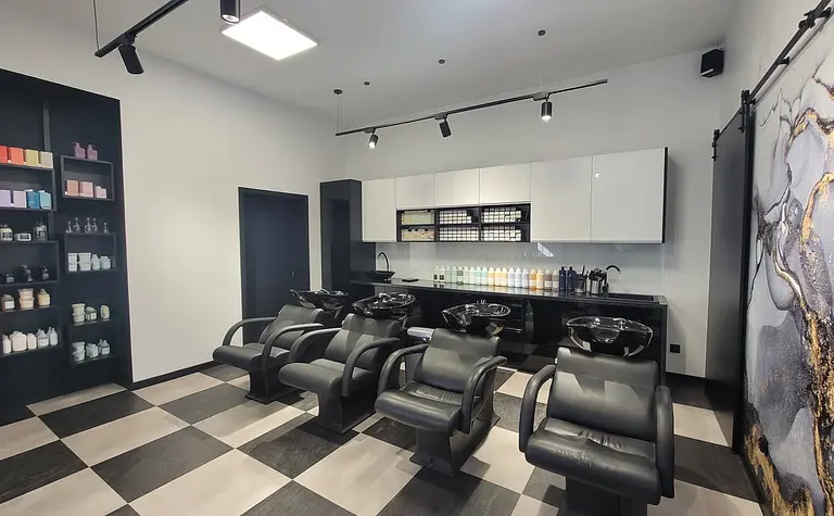Salon fryzjerski z czarnymi fotelami i kosmetykami na półkach, styl industrialny i nowoczesny.