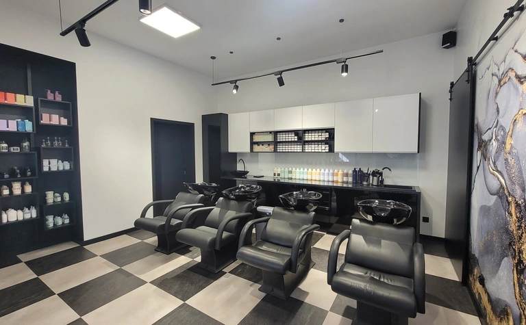 Salon fryzjerski z czarnymi fotelami i kosmetykami na półkach, styl industrialny i nowoczesny.