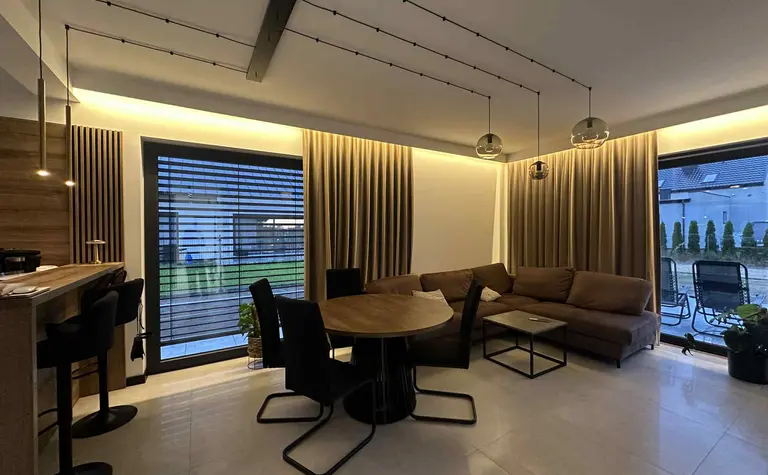 Nowoczesny salon z brązową sofą, drewnianym stołem i industrialnym oświetleniem.