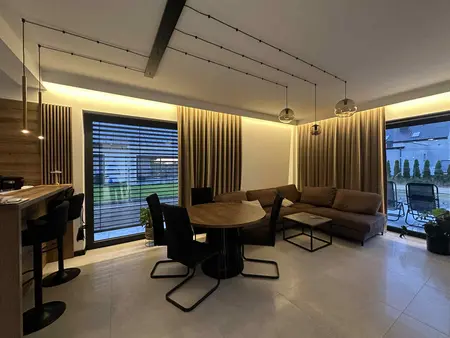 Nowoczesny salon z brązową sofą, drewnianym stołem i industrialnym oświetleniem.