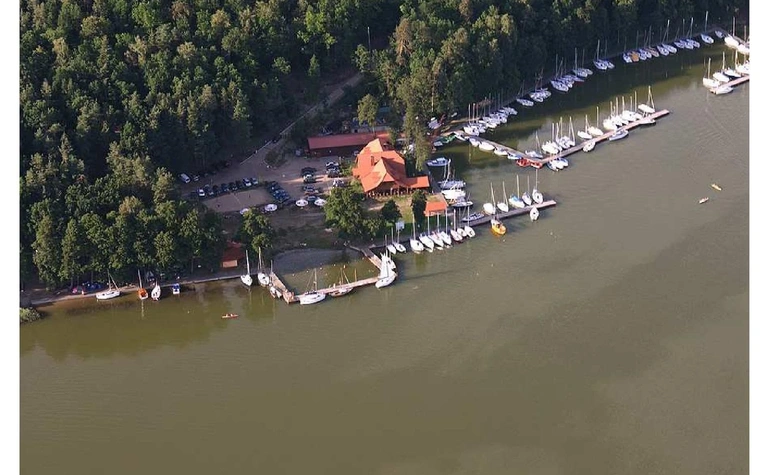 Widok portu z jachtami i drewnianym domkiem otoczonym zielenią. Minimalistyczny i nowoczesny styl.