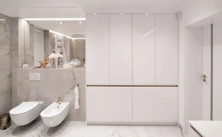 Nowoczesna łazienka glamour z białymi meblami i złotymi detalami.