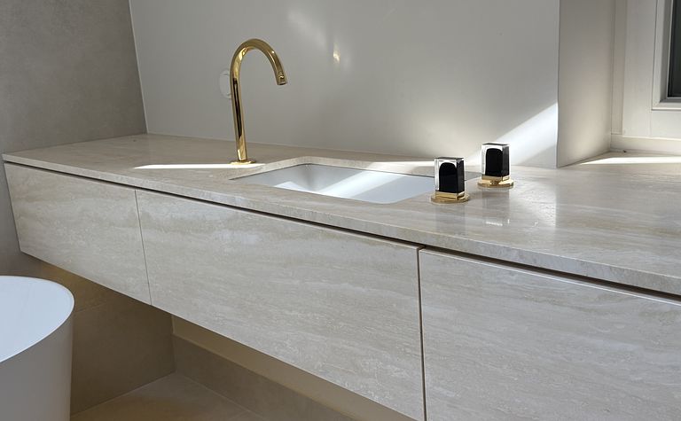 Jasna łazienka z blatem z trawertynu i złotymi bateriami ze szlanymi uchwytami by wedodesign.pl