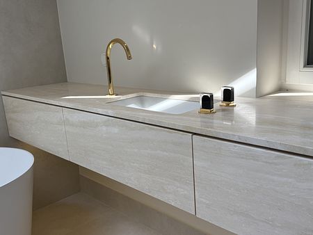 Jasna łazienka z blatem z trawertynu i złotymi bateriami ze szlanymi uchwytami by wedodesign.pl