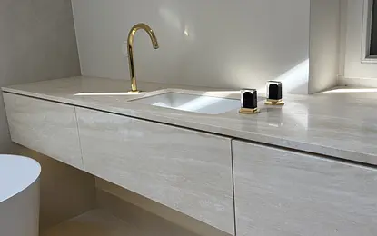 Jasna łazienka z blatem z trawertynu i złotymi bateriami ze szlanymi uchwytami by wedodesign.pl