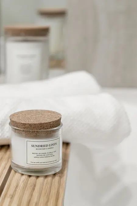 Nowoczesna łazienka z białą świecą i ręcznikami na drewnianej półce.