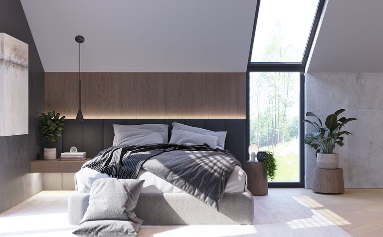 Wnętrze sypialni z szarym łóżkiem, drewnianymi detalami i dużymi oknami, minimalistyczny styl.
