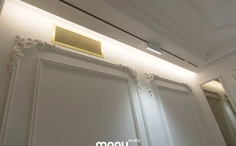 Stylowe wnętrze z białymi ścianami, złotymi akcentami i klasycznymi detalami.
