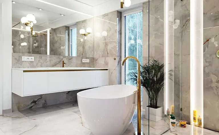 Nowoczesna łazienka glamour z białą wanną i złotymi detalami.