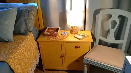 Wnętrze sypialni z żółtym stolikiem, szarymi zasłonami i rustykalnymi akcentami.