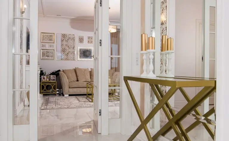 Przedpokój z lustrem, złotą konsolą i designerskim oświetleniem w stylu glamour oraz quiet luxury.