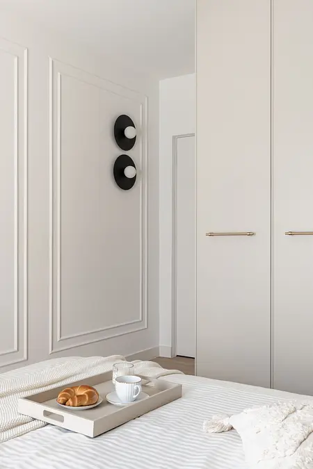 Sypialnia z białymi meblami, czarnymi lampami i kocem.