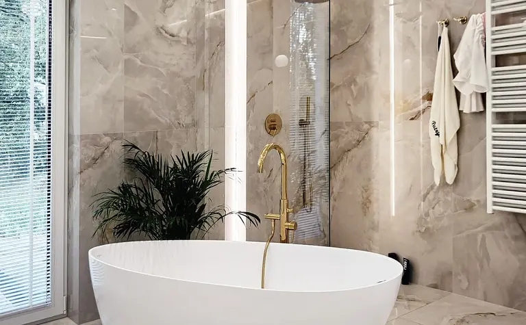 Nowoczesna łazienka glamour z białą wanną i złotymi detalami.