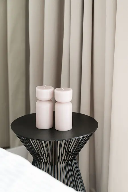 Współczesna sypialnia z różowymi świecami na czarnym stoliku i jasnymi zasłonami.