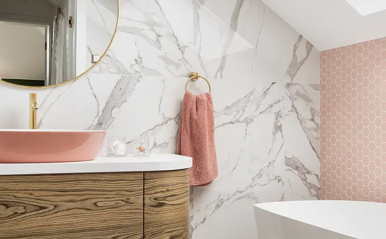 Wnętrze łazienki z elementami art deco, boho i glamour, w tym drewniana szafka i różowa umywalka.