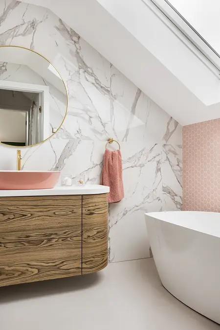 Wnętrze łazienki z elementami art deco, boho i glamour, w tym drewniana szafka i różowa umywalka.
