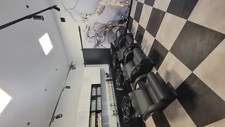 Salon fryzjerski z czarnymi fotelami i nowoczesnym wystrojem.