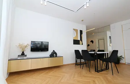 Wnętrze jadalni z drewnianym stołem, czarnymi krzesłami i nowoczesnymi dekoracjami.