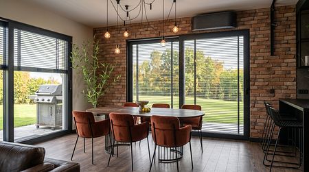 Wnętrze jadalni z okrągłym stołem, brązowymi krzesłami i ścianą z cegły, styl industrialny i współczesny.