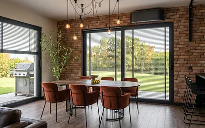 Wnętrze jadalni z okrągłym stołem, brązowymi krzesłami i ścianą z cegły, styl industrialny i współczesny.