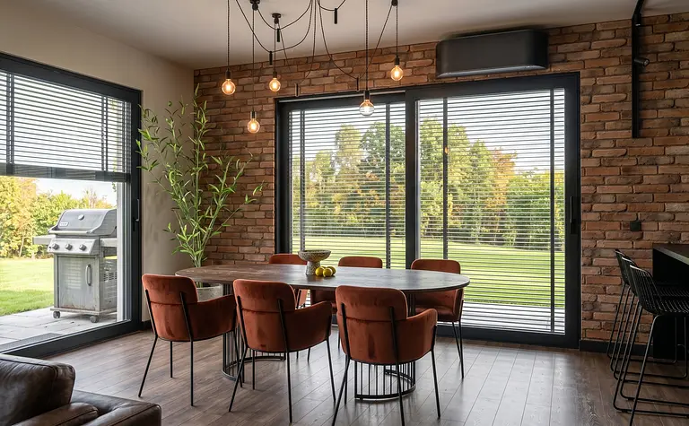 Wnętrze jadalni z okrągłym stołem, brązowymi krzesłami i ścianą z cegły, styl industrialny i współczesny.