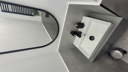 Minimalistyczna toaleta z białą umywalką, czarnym lustrem i szarymi płytkami.