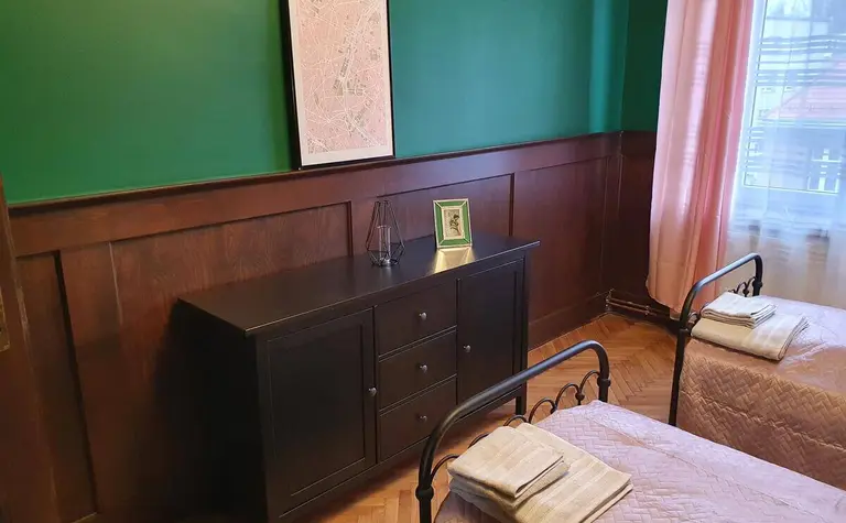 Tradycyjny pokój z zieloną ścianą, drewnianymi meblami i różowymi kołdrami.