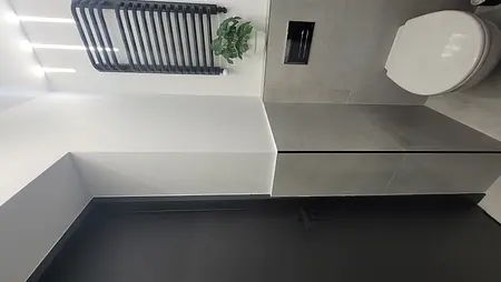 Toaleta w stylu minimalistycznym z szarymi płytkami, czarnymi akcentami i rośliną.