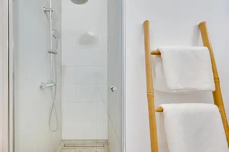 Nowoczesna łazienka z prysznicem i białymi ręcznikami na bambusowym regałku, styl japandi.