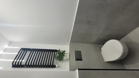 Minimalistyczna toaleta z szarymi płytkami i białą miską.
