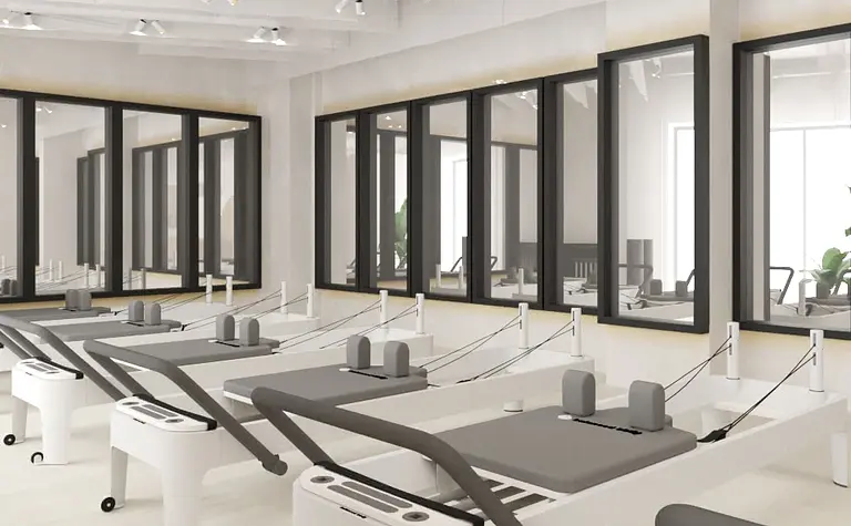 Studio pilates z białymi maszynami i dużymi oknami, soft minimalizm