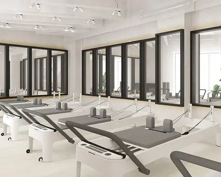Studio pilates z białymi maszynami i dużymi oknami, soft minimalizm